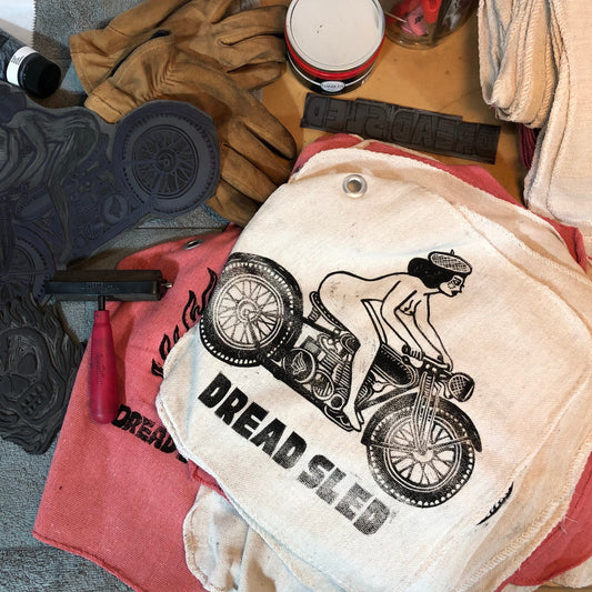 Shop towl with motorcycle graphic and 'Dread Sled' text on a workbench with tools and materials.